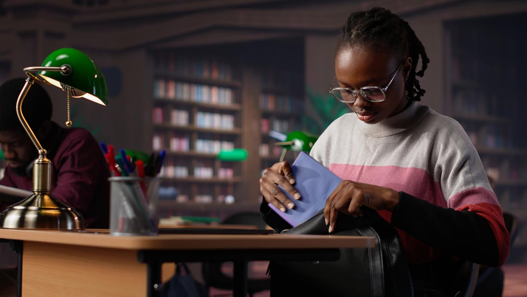 A student packing a book into her backpack in a university library